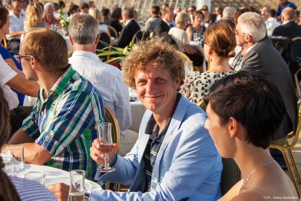 Happy man at dinner table on deck with a crowd of dinner guest